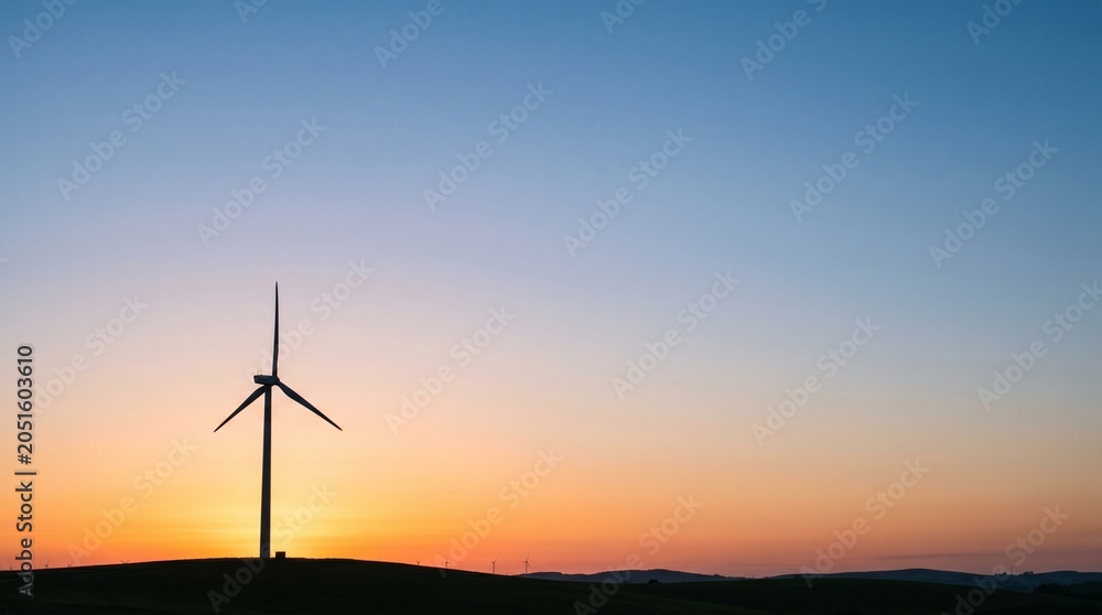 Obraz premium Silhouette of a wind turbine against a gradient sunset sky with rolling hills