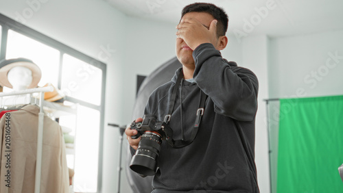 Cuadro en lienzo Man with camera adjusts the lens and briefly covers his face with a hand in a studio while checking settings; frustration troubleshooting