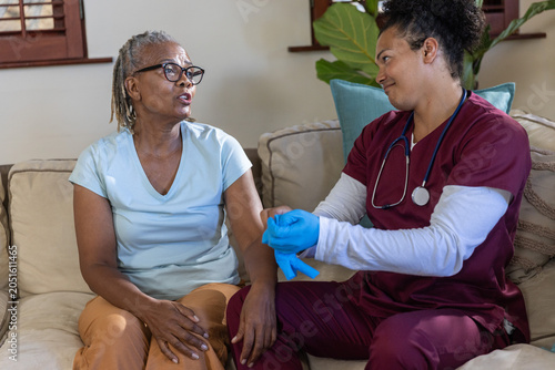 Εκτύπωση καμβά Senior African American woman sitting on couch at home while nurse pulling blue