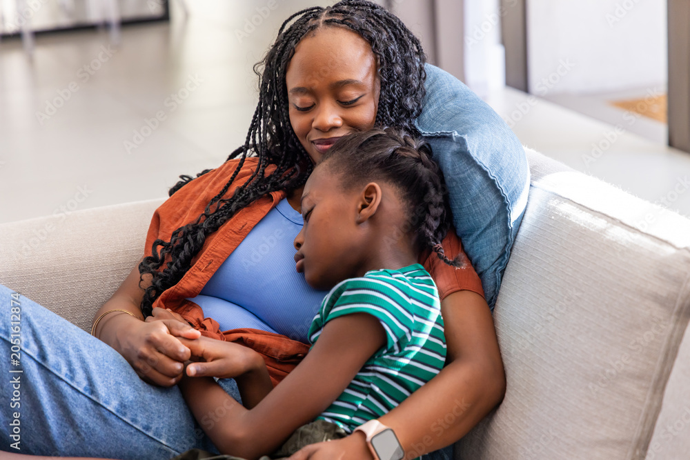 Obraz premium African mother and child resting on light sofa in living room, wearing blue top and smartwatch