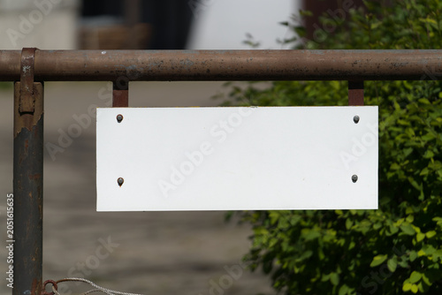leeres, weißes, unbeschriftetes Schild mit Platz für eigenen Text an einem Zaun