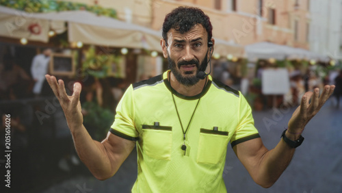 Quadro su tela Man referee with whistle raising hands and shrugging on a street market, headset mic and neon shirt visible; frustration appeal