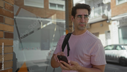 Foto Man with glasses and backpack briefly tapping smartphone at a storefront window on a street; quiet concern