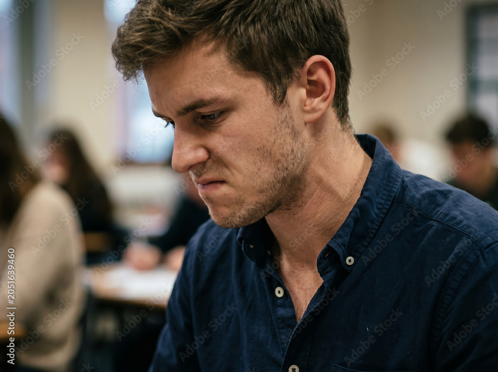 Obraz premium Pensive male student looking down at book or exam paper