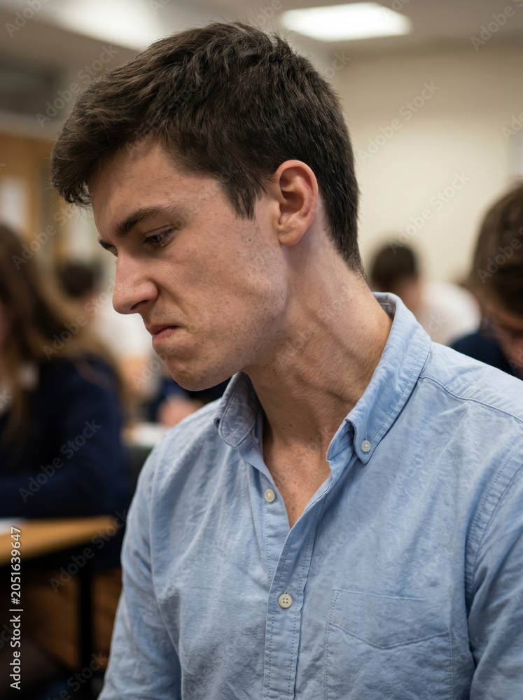 Fototapeta premium Disappointed young man looking down with sad expression in classroom
