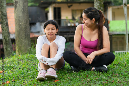 Laughing Latina mother listening to her daughter while sharing a joyful moment on the grass