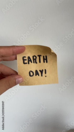 Hand holding kraft paper note with handwritten Earth Day message on white background