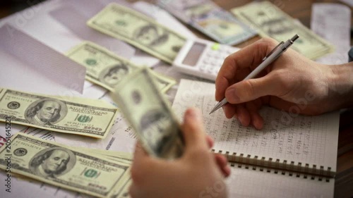 An entrepreneur meticulously records financial indicators in a diary, surrounded by dollar bills, a calculator, and important documents, showcasing careful financial planning and accounting practices