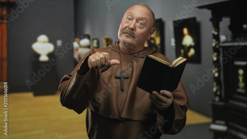 Schilderij op canvas Man holding bible and wearing cross, thumb pointing to self while reading in a museum building; faith reflection serenity
