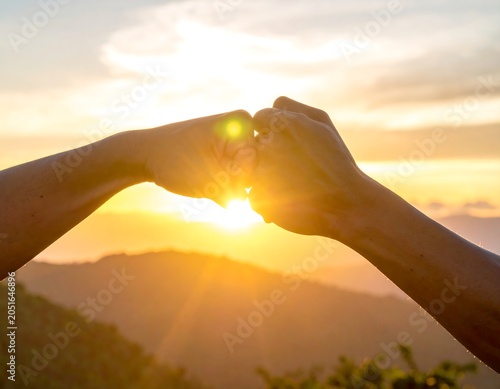A serene sunset scene with two hands forming a heart shape
