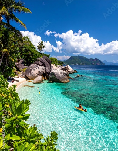 A serene tropical beach with crystal-clear turquoise water, large rocks, and lush greenery under a bright blue sky with white clouds