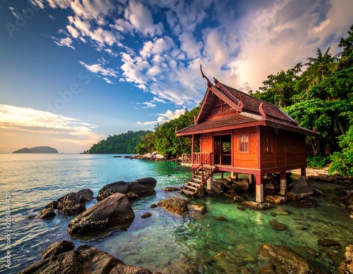 A serene tropical hut on stilts over crystal-clear waters with a vibrant blue sky and lush greenery