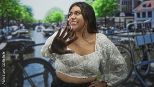 Slika na platnu Woman showing midriff and reaching hand forward on street with canal and bicycles nearby; playful confidence