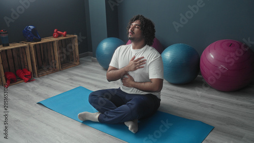 Foto Man seated crosslegged on blue yoga mat with hand on chest and breathing in studio; mindfulness calm