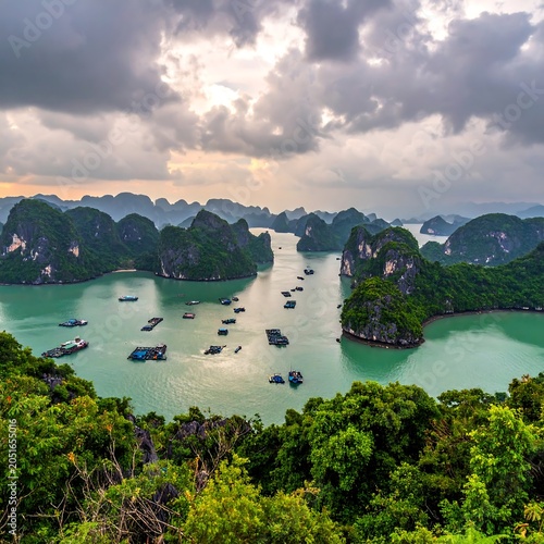 A serene turquoise bay surrounded by lush green mountains and scattered boats under a dramatic cloudy sky