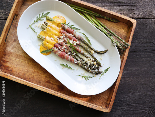 Roasted prosciutto wrapped asparagus with  sauce on a white platter