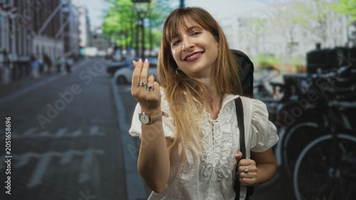 Фотография Woman beckons with hand and fingers while holding a guitar case on a busy city street lined with bicycles and parked cars; playful