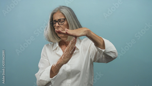 Photos Woman with grey hair making a timeout hand gesture with palms raised and crossed in a light blue studio; frustration refusal boundary setting