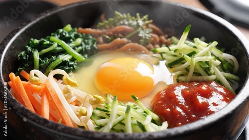 Traditional Korean bibimbap with fresh vegetables and raw egg yolk served in a hot stone bowl