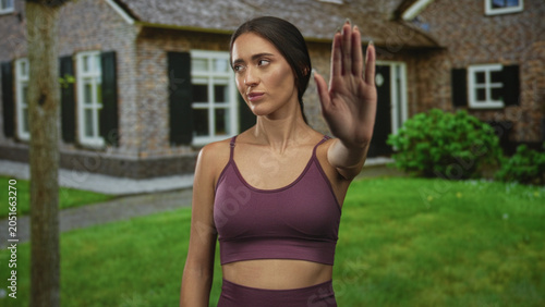 Foto Woman with hand raised palm out at house entrance building, wearing maroon sports bra and midriff visible while giving a stop gesture; rejection privacy boundary