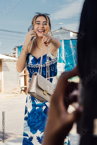 Foto Alegre mujer hispana con vestido floral hablando por celular y apuntando a la cámara en un parque urbano