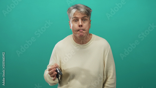 Принти на полотні Man holding car key fob in one hand, puckering lips and shrugging before a teal studio wall; mild confusion