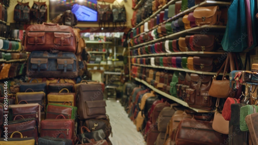 Fototapeta premium Defocused leather bag display and stacked backpacks in a blurred shop aisle interior; background backplate template calm.