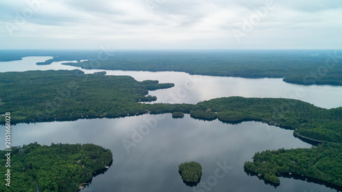 An expansive high-angle drone photograph capturing a vast panoramic view of Lake of Bays, featuring dense green forested islands, winding shorelines, and calm waters under an overcast spring sky.