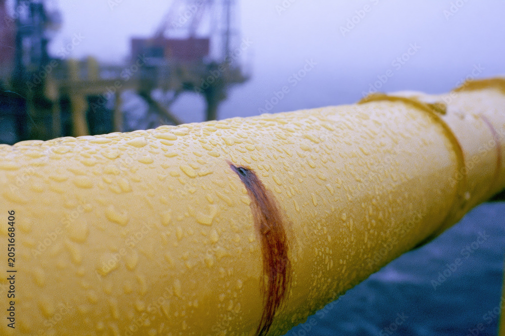 Obraz premium Yellow pipe rain droplet rust spot industrial railing offshore rig misty background harsh daylight macro detail metal surface wet texture