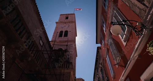 Historic stone clock tower rising above a narrow street lined with traditional buildings in the old town of Sibenik Croatia.