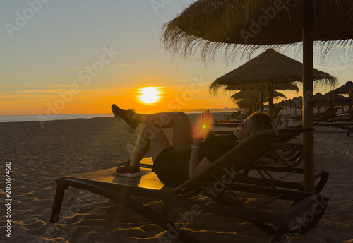 Beautiful middle-aged woman sitting on sandy beach on sunset on spring day. Back view. beach on Algarve coast in Portugal