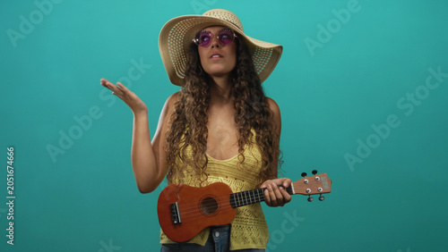 Foto Hispanic woman playing ukulele with right hand gesturing and left hand on frets in studio; carefree joy