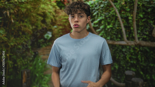 Foto Teenage boy gesturing with hands while speaking in forest walkway with wooden railing and dense foliage; thoughtful reflection