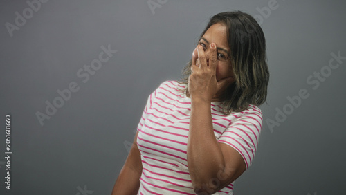 Photography Woman covering face with hand and peeking through fingers in studio wearing pink striped t shirt; shyness privacy