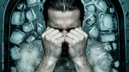 Top-down view of man submerged in cold ice bath holding fists to face