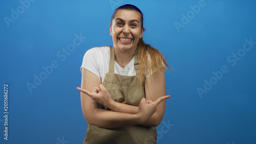 Fényképezés Woman in apron and white tshirt points both index fingers crosswise while smiling toward side in studio; playfulness humor