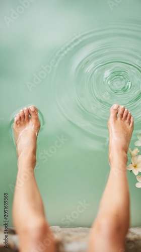 Relaxed legs soak in turquoise spa water with floating plumeria flowers. Gentle ripples create a serene, tranquil atmosphere for wellness and calm.
