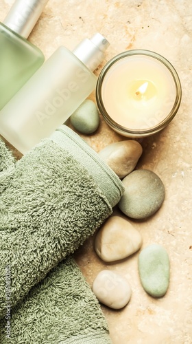 Minimalist spa still life with sage towels, river stones, and a glowing candle. Soft green and creamy tones evoke luxury wellness and tranquil, restorative interiors.