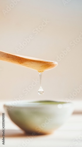 A minimalist wooden spoon holds a single drop of oil above a ceramic bowl. Soft shadows and natural tones evoke high-end spa aesthetics and tranquil craftsmanship.
