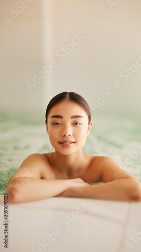 A serene wellness scene captures a relaxed woman immersed in warm water at a minimalist spa. Soft daylight and subtle hues evoke luxury, balance, and tranquility.