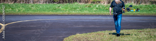 Tableau sur toile Cinematic panoramic shot of an anonymous RC pilot carrying a scale model warbird fighter airplane along an airfield runway with vast text copy space