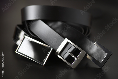 Three black leather belts with diverse decorative buckles.