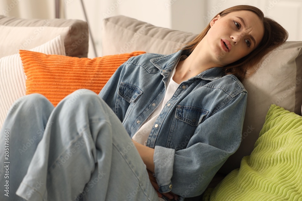 Obraz premium Young woman suffering from menstrual pain on sofa at home