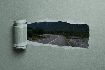 Mountain road, view through hole in torn pastel green paper