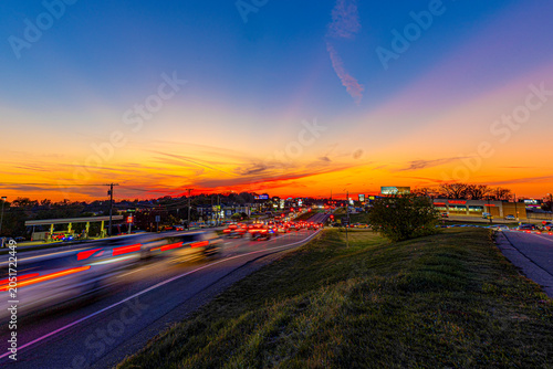 Taillights glowing as they pass under a bright sunset