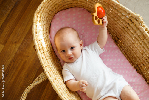 Tableau sur toile Baby girl raising wooden teether while lying in wicker bassinet