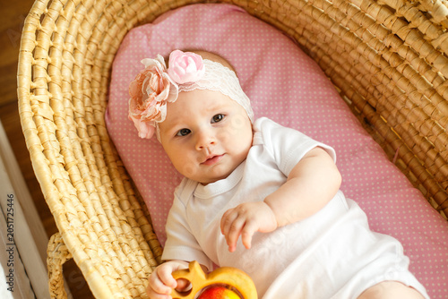 Fotografie Baby girl with floral headband resting in wicker bassinet