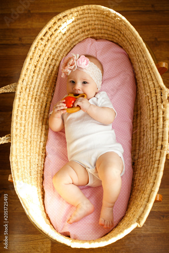 Fotografie Baby girl chewing wooden teether while lying in wicker bassinet