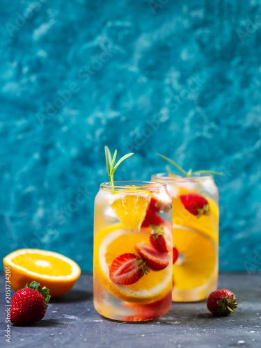 Two glasses of Refreshing cold summer detox drink with orange and strawberry. Blue background