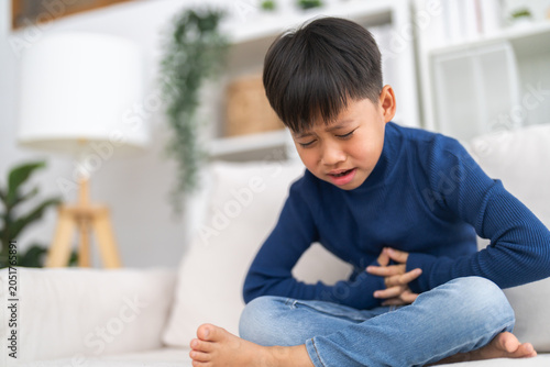Foto Portrait of sick unhappy little child asian boy touching belly stomach with suff